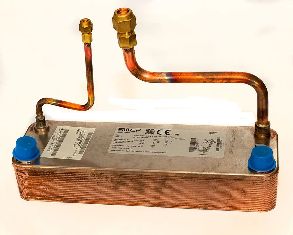 Kupferne Wärmeübertragungseinheit mit zwei Anschlussrohren und Kappen in Blau, verwendet in Daikin Heizsystemen. Beschriftung und technische Informationen auf der Oberseite sichtbar.